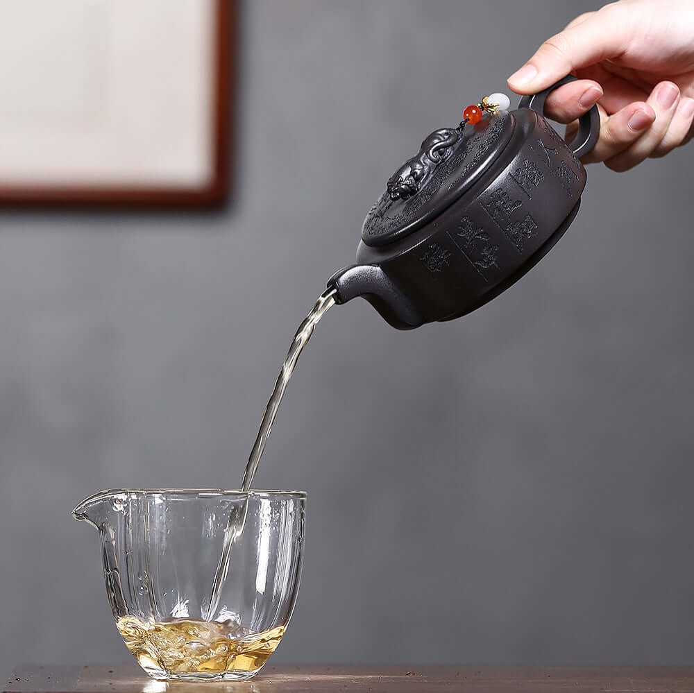 Handmade Yixing purple sand teapot pouring tea into glass cup, ideal for Kung Fu tea set and home use.