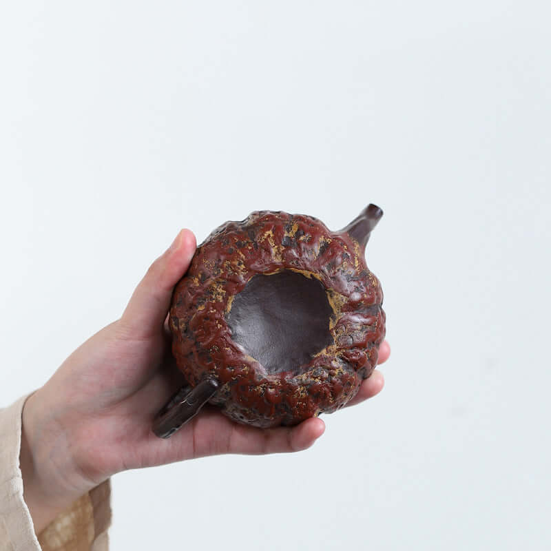 Handmade Yixing purple sand pumpkin teapot held in a hand, showcasing intricate design and craftsmanship.