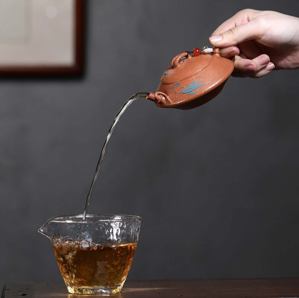 Handmade Yixing purple sand teapot pouring tea into a glass cup, showcasing traditional Kung Fu tea ceremony.