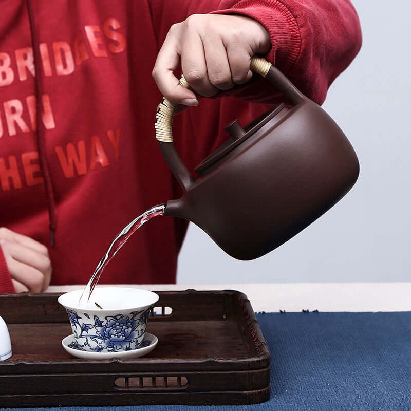 Handmade Yixing purple sand teapot pouring water into a traditional Chinese tea cup, demonstrating elegance and craftsmanship.