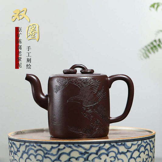 Handmade Yixing purple sand teapot featuring intricate bird engravings on a dark brown surface.