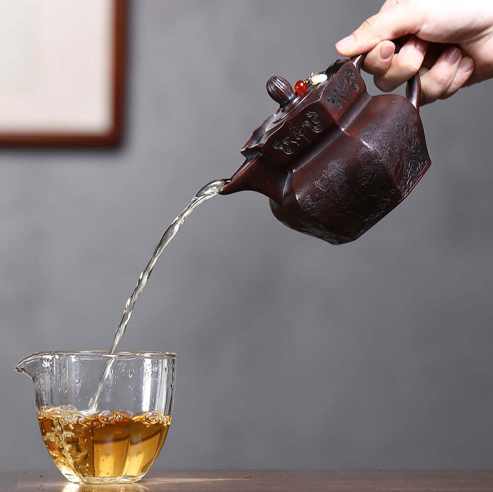 Handmade Yixing purple sand teapot pouring tea into a glass cup, showcasing craftsmanship and elegance for Kung Fu tea.