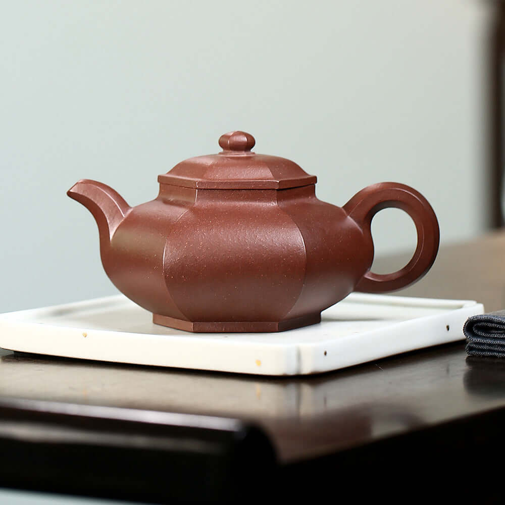 Handmade Yixing purple sand teapot on a white tray, showcasing elegant design and craftsmanship.