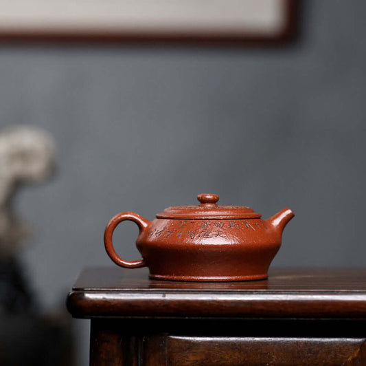 Handmade Yixing purple sand teapot on wooden table, showcasing its unique craftsmanship and engraved design.