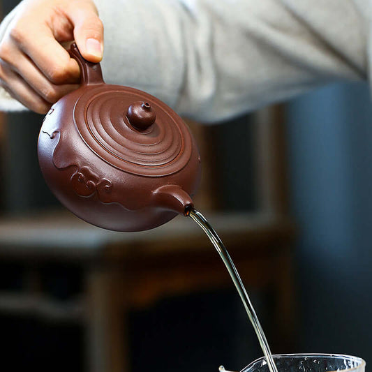 Handmade Yixing purple sand teapot pouring water with intricate design, showcasing craftsmanship and elegance.