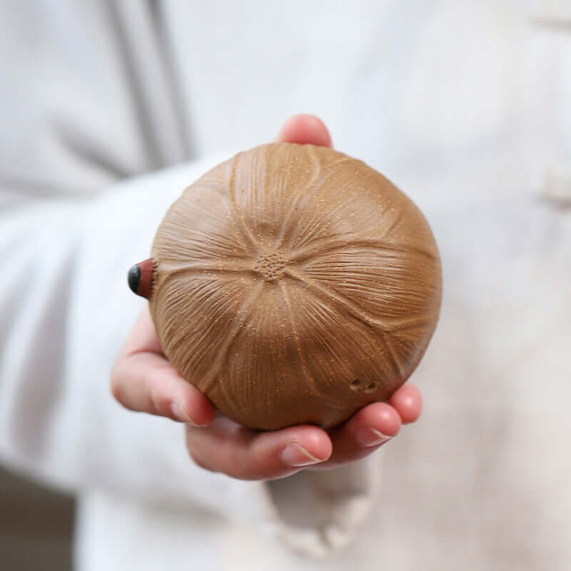 Handmade Yixing purple clay tea cup in a person's hand, showcasing fine craftsmanship and unique texture.