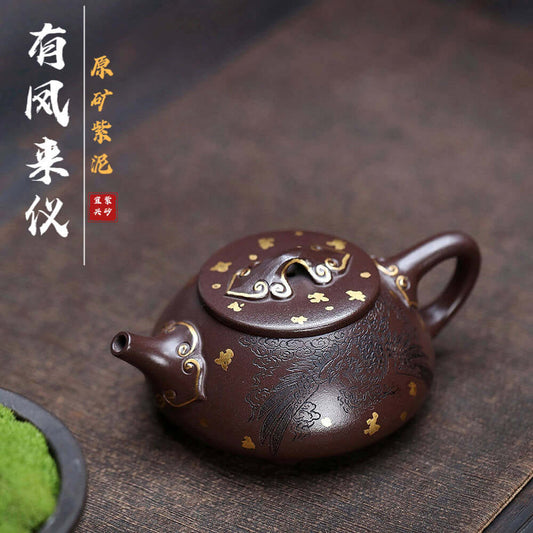 Handmade Yixing purple sand teapot with gold accents, featuring intricate phoenix design, showcasing traditional craftsmanship.