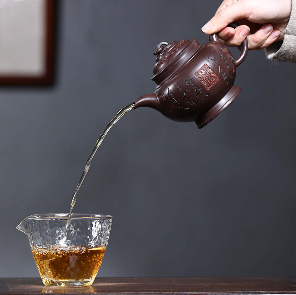 Handmade Yixing purple sand teapot pouring tea into a glass cup, showcasing artisanal craftsmanship and elegance.