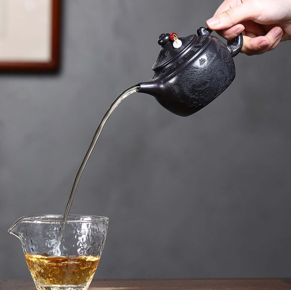 Handmade Yixing purple sand teapot pouring tea into a glass cup, showcasing craftsmanship and elegance.
