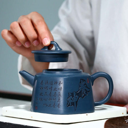 Handmade Yixing purple sand teapot with intricate carvings and lid being placed on top, showcasing fine craftsmanship.