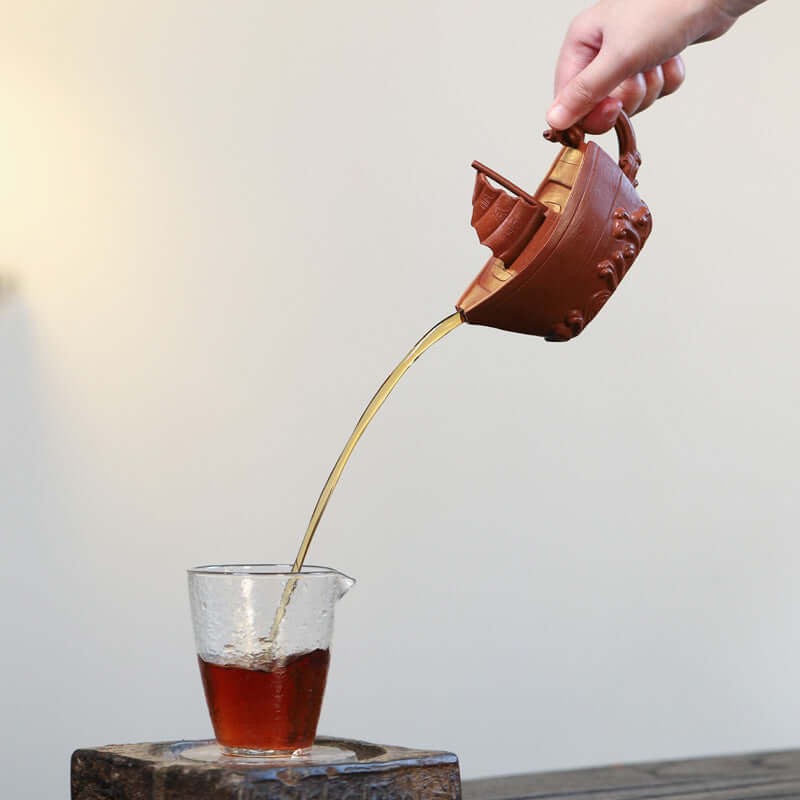 Handmade Yixing purple sand teapot pouring tea into a glass cup, showcasing its unique craftsmanship and design.