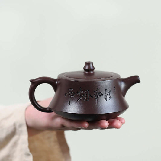 Handmade Yixing purple sand teapot featuring traditional Chinese calligraphy design, held in a hand.