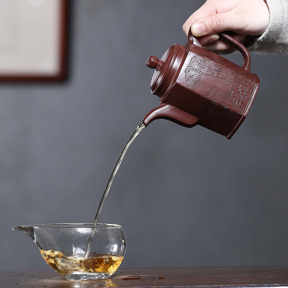 Handmade Yixing purple sand teapot pouring tea into glass cup, showcasing craftsmanship of original purple clay.
