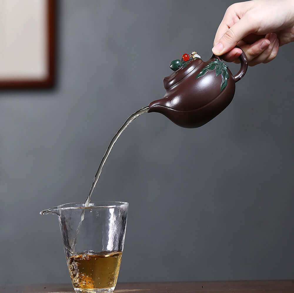 Handmade Yixing purple sand teapot pouring tea into a glass, showcasing the craftsmanship of a two-tone peach-shaped design.