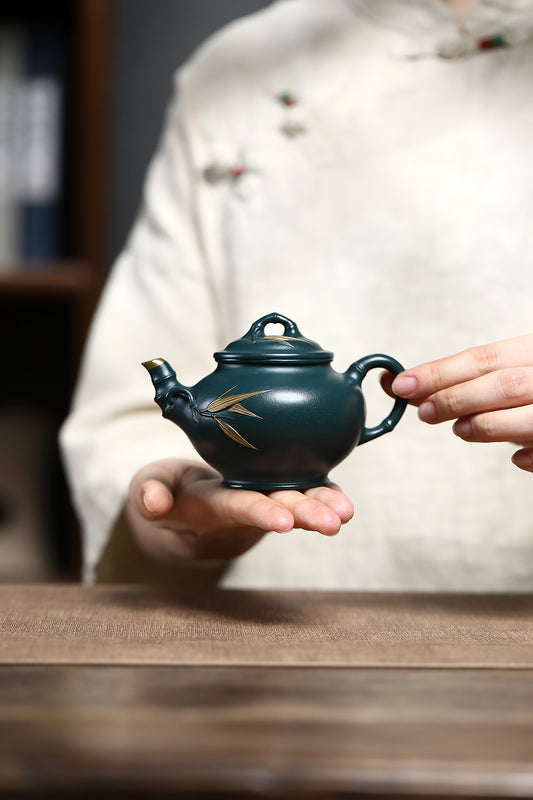 Handmade Yixing purple sand teapot featuring bamboo design held delicately in hand, showcasing its unique craftsmanship.