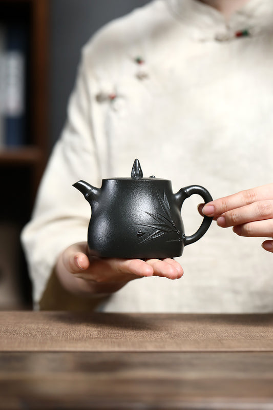 Handmade Yixing purple sand teapot with bamboo design, held by a person wearing traditional attire.