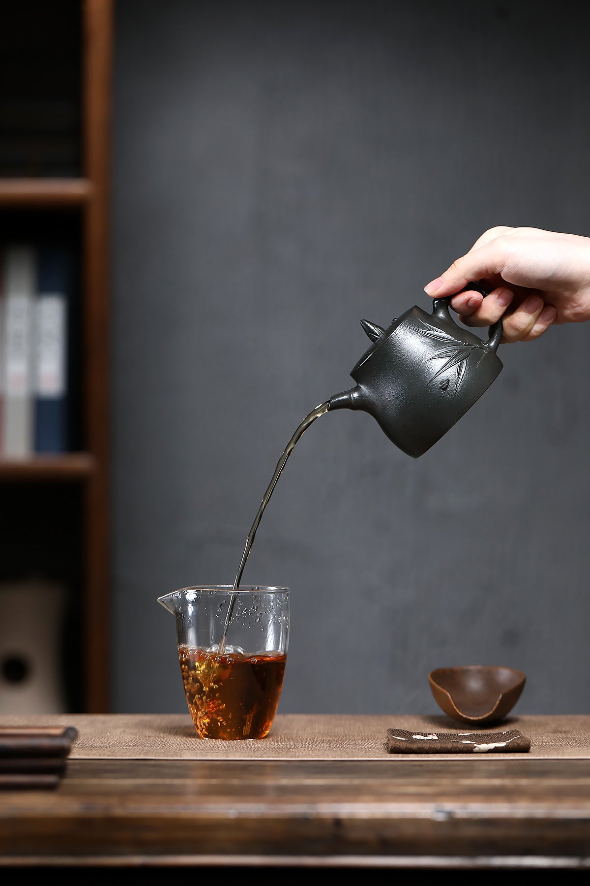 Handmade Yixing purple sand teapot pouring tea into a clear cup on a wooden table.