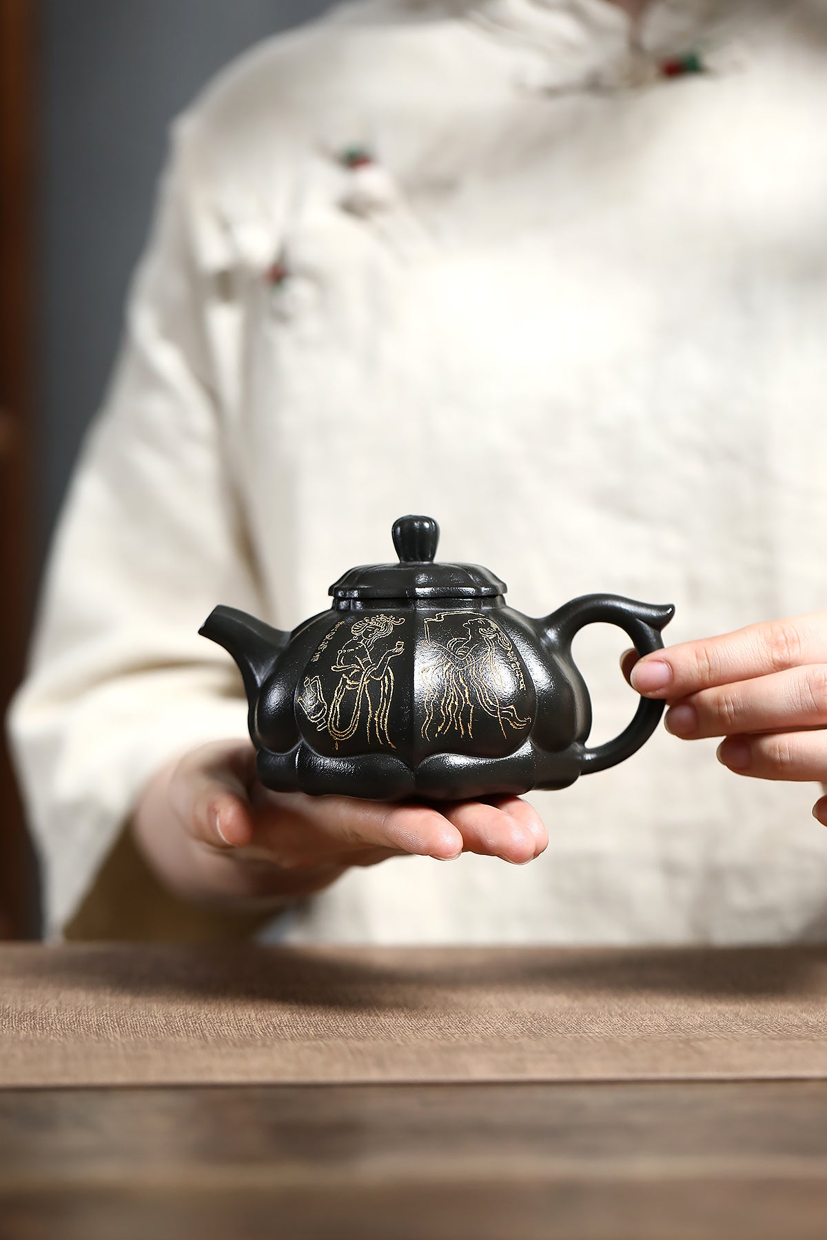 Handmade Yixing purple sand teapot with intricate gold detailing, held by artisan against neutral backdrop.