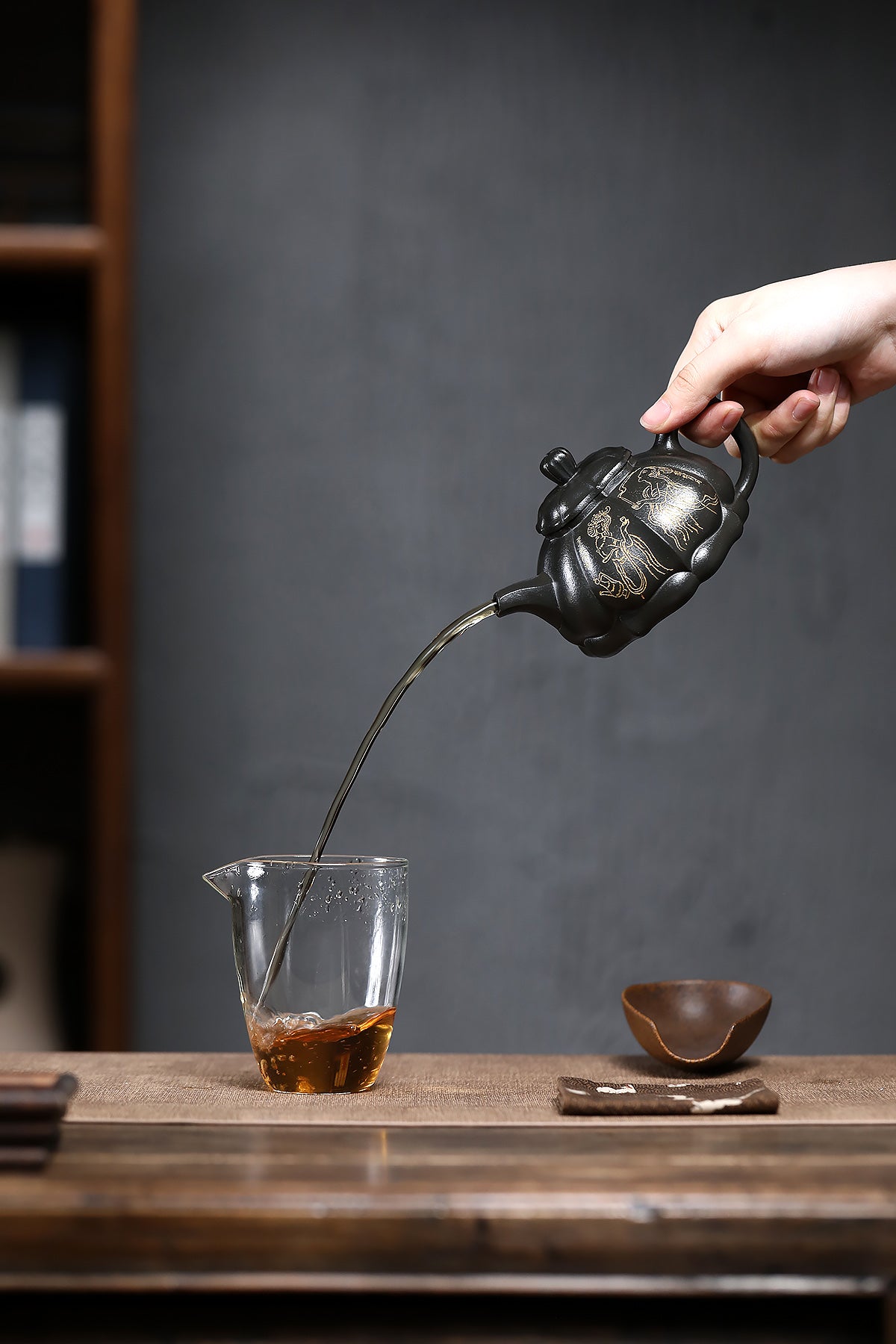 Handmade Yixing purple sand teapot pouring tea into a clear glass, showcasing elegant craftsmanship and traditional tea culture.