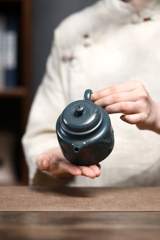 Handmade Yixing purple sand teapot, held in a person's hand, showcasing its unique design and craftsmanship.