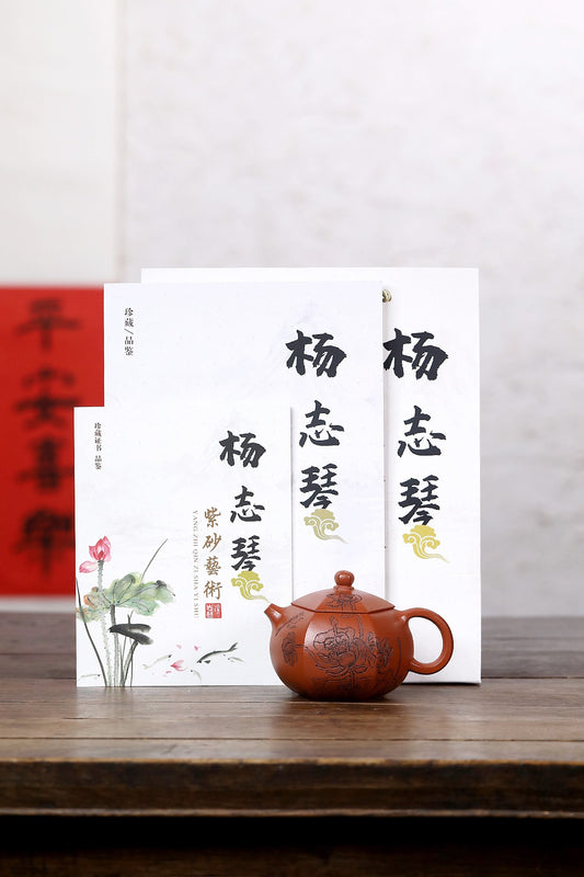 Handmade Yixing purple sand teapot displayed with traditional calligraphy books on a wooden table.
