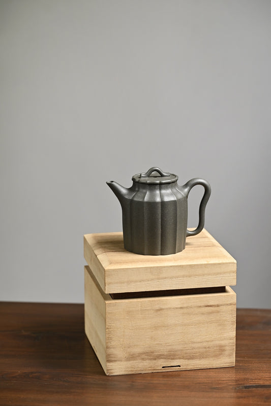 Handmade Yixing purple sand teapot on a wooden box, showcasing elegant lines and craftsmanship.