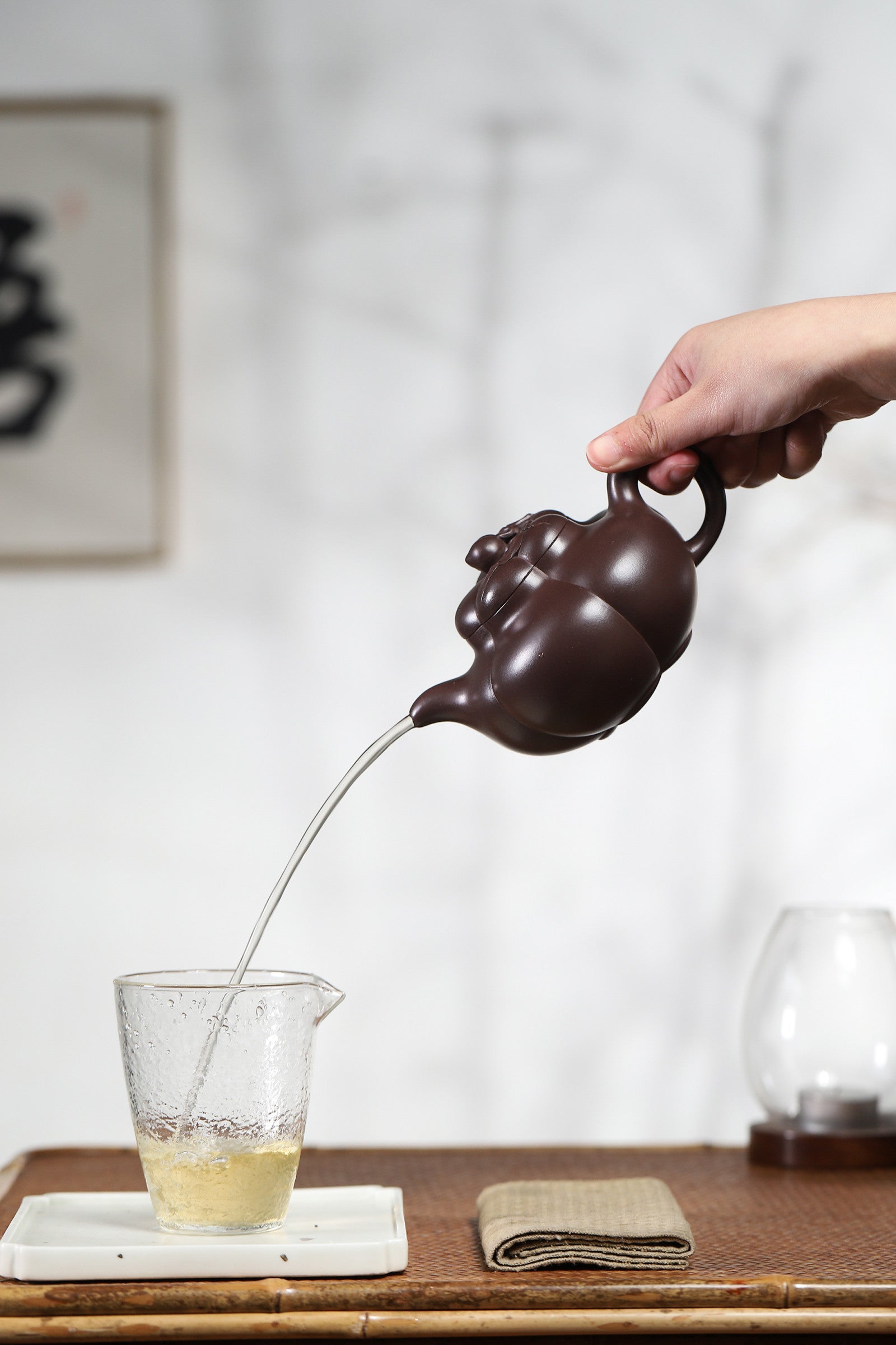 Handmade Yixing purple sand teapot pouring tea into glass, showcasing its elegant design and craftsmanship.