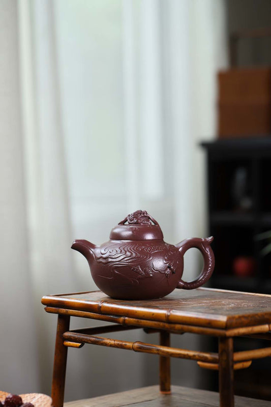 Handmade Yixing purple sand teapot, featuring intricate dragon design, on a wooden table in a bright room.
