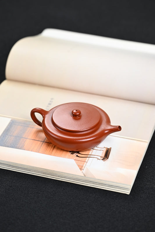 Handmade Yixing purple sand teapot resting on an open book, showcasing its elegant design.