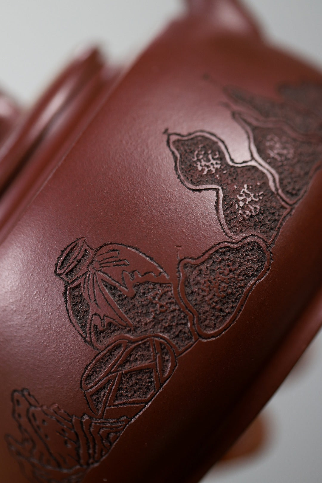 Close-up of a handmade Yixing purple sand teapot featuring detailed engravings of traditional motifs.