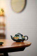Chinese purple clay teapot with gold and silver inlay displayed on a wooden table.