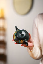 Chinese purple clay teapot with gold and silver inlay held in hand, showcasing intricate design and craftsmanship.