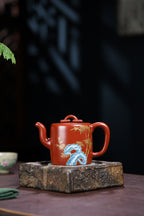 Handmade enamel tea pot displayed on a wooden pedestal, showcasing intricate bamboo design and vibrant colors.