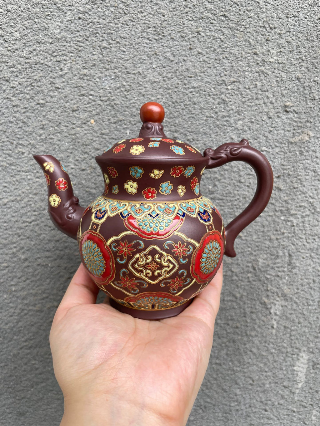 Yixing purple clay teapot with enamel decoration in hand, showcasing beautiful floral patterns and rich colors.