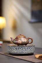 Yang Junbao handcrafted Zhisha teapot resting on a decorative plate, featuring intricate floral designs and a warm ambiance.