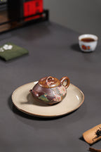Yang Junbao handcrafted Zhisha teapot displayed on a plate, featuring intricate floral designs and a traditional design.