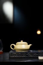 Handcrafted Yixing teapot with cat decoration on a textured tray in a dimly lit setting.