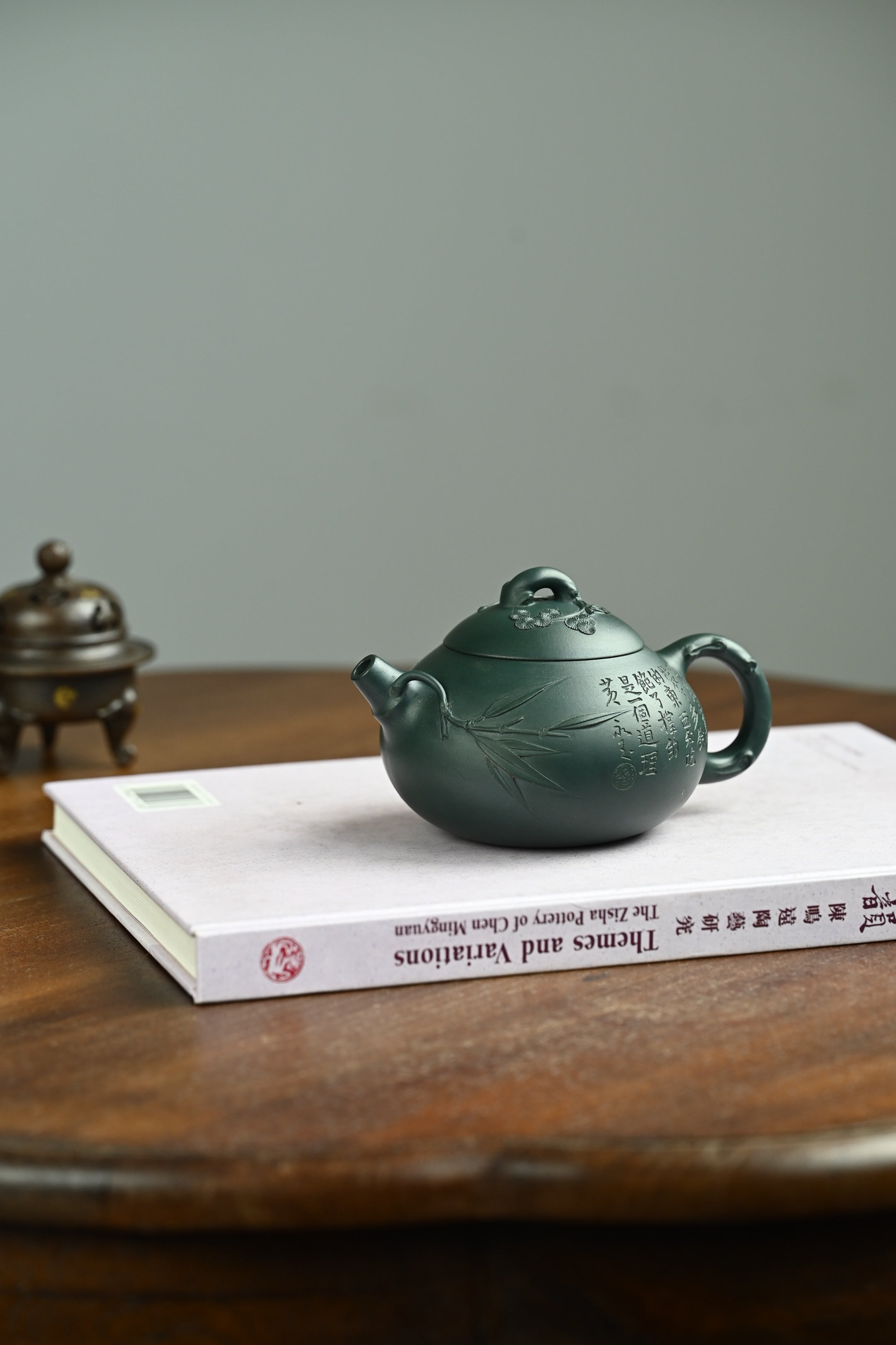 喜乐生财·全手工/容量280cc/一厂墨绿泥 壶身圆润饱满，片片竹叶覆于壶身之上，盖面松针坚韧，梅花傲然绽放